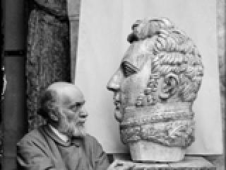 Antoine Bourdelle (1861-1929), assis près de la tête monumentale du Général "Alvear". Photographie anonyme. Paris, musée Bourdelle.